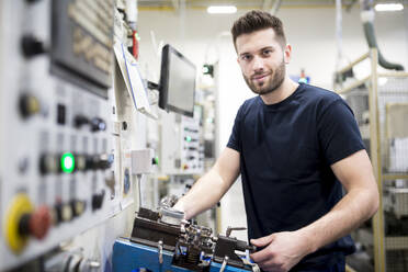 Porträt eines selbstbewussten Mannes, der in einer modernen Fabrik an einer Maschine arbeitet - WESTF24247