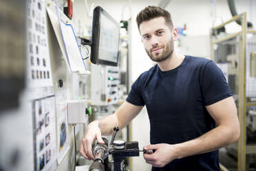 Porträt eines selbstbewussten Mannes, der in einer modernen Fabrik arbeitet und eine Maschine bedient - WESTF24257