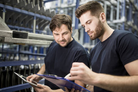 Zwei Arbeiter mit Klemmbrett und Tablet in einem Fabriklager, lizenzfreies Stockfoto