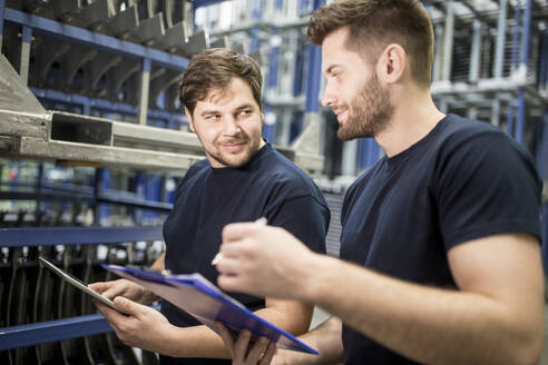 Zwei Arbeiter mit Klemmbrett und Tablet in einem Fabriklager - WESTF24274