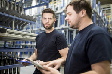 Zwei Arbeiter mit Klemmbrett und Tablet in einem Fabriklager - WESTF24276