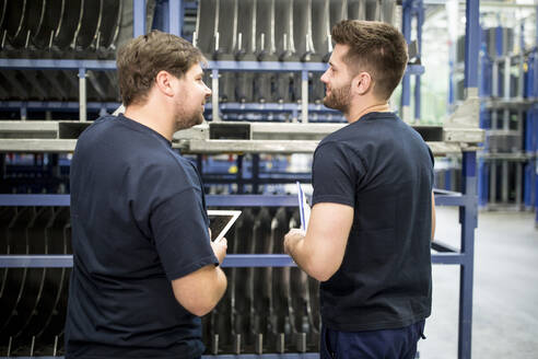 Zwei Arbeiter mit Klemmbrett und Tablet in einem Fabriklager - WESTF24278