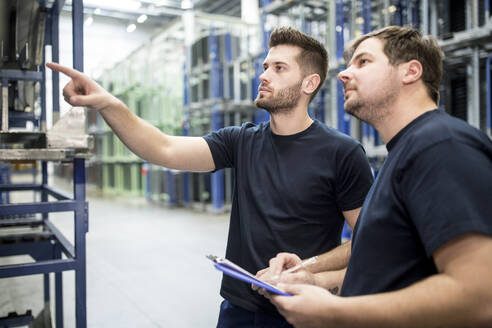 Arbeiter mit Kollege in einem Fabriklager, der mit dem Finger zeigt - WESTF24279