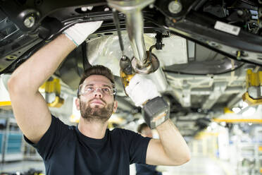 Mann arbeitet am Unterboden eines Autos in einer modernen Fabrik - WESTF24340