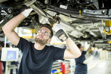 Zwei Kollegen arbeiten in einer modernen Fabrik am Unterboden eines Autos - WESTF24341