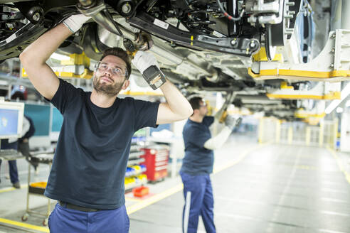 Zwei Kollegen arbeiten in einer modernen Fabrik am Unterboden eines Autos - WESTF24342