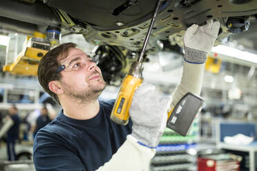 Mann arbeitet am Unterboden eines Autos in einer modernen Fabrik - WESTF24343