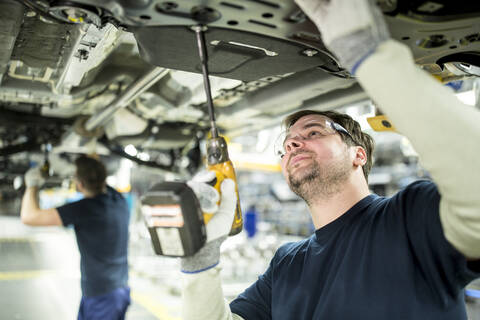 Zwei Kollegen arbeiten in einer modernen Fabrik am Unterboden eines Autos, lizenzfreies Stockfoto