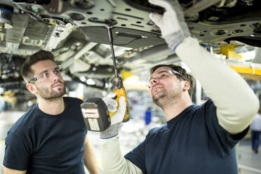 Zwei Kollegen arbeiten in einer modernen Fabrik am Unterboden eines Autos - WESTF24345