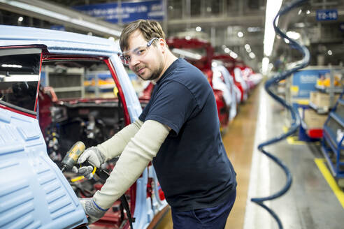 Porträt eines selbstbewussten Mannes, der in einer modernen Autofabrik arbeitet - WESTF24366