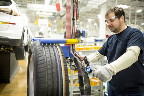 Mann arbeitet an einem Reifen in einer modernen Autofabrik - WESTF24382