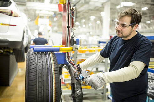 Mann arbeitet an einem Reifen in einer modernen Autofabrik - WESTF24383