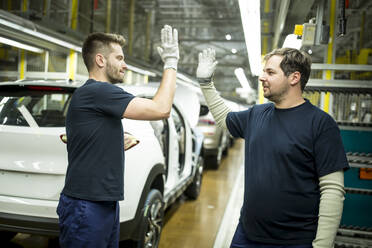 Zwei Kollegen, die sich in einer modernen Autofabrik die Hände reichen - WESTF24387