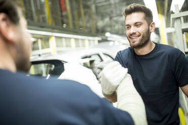 Zwei Kollegen beim Händeschütteln in einer modernen Autofabrik - WESTF24390