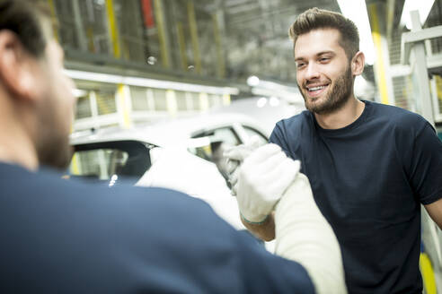 Zwei Kollegen beim Händeschütteln in einer modernen Autofabrik - WESTF24390