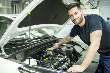 Porträt eines selbstbewussten Mannes, der in einer modernen Fabrik an einem Auto arbeitet - WESTF24391