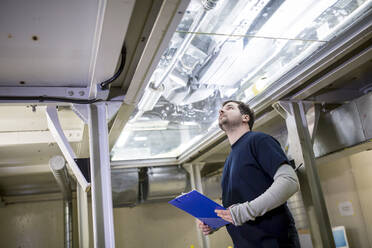 Mann in der Fabrik bei der Kontrolle des Unterbodens eines Autos - WESTF24396