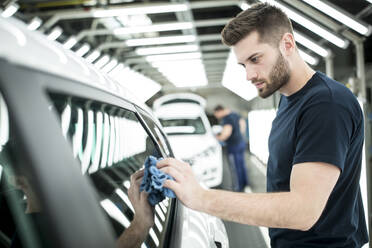 Mann arbeitet in einer modernen Autofabrik und wischt ein fertiges Auto ab - WESTF24401