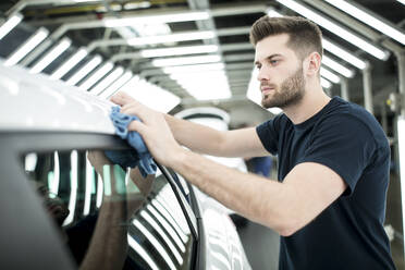 Man working in modern car factory wiping finished car - WESTF24402