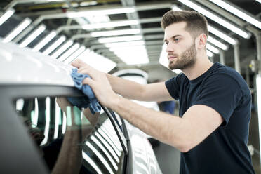 Mann arbeitet in einer modernen Autofabrik und wischt ein fertiges Auto ab - WESTF24402