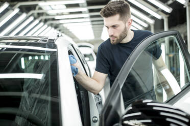 Mann arbeitet in einer modernen Autofabrik und wischt ein fertiges Auto ab - WESTF24403