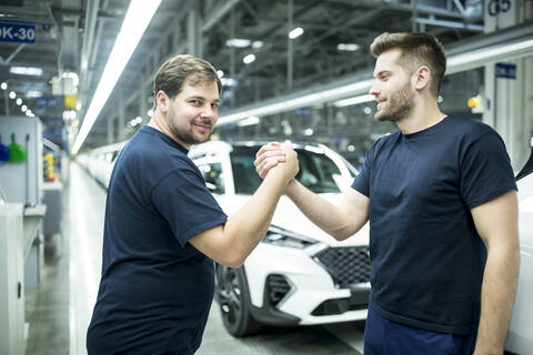 Zwei Kollegen beim Händeschütteln in einer modernen Autofabrik, lizenzfreies Stockfoto