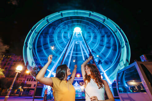 Two friends with sparkles in front of illuminated big wheel at night - MTBF00086