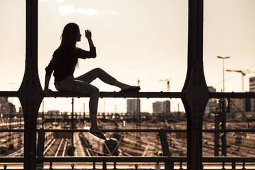 Junge Frau sitzt bei Sonnenuntergang auf der Hackerbrücke, München, Deutschland - WFF00124