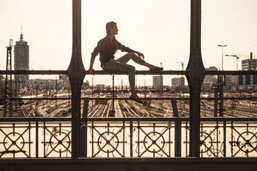 Junge Frau sitzt bei Sonnenuntergang auf der Hackerbrücke, München, Deutschland - WFF00125