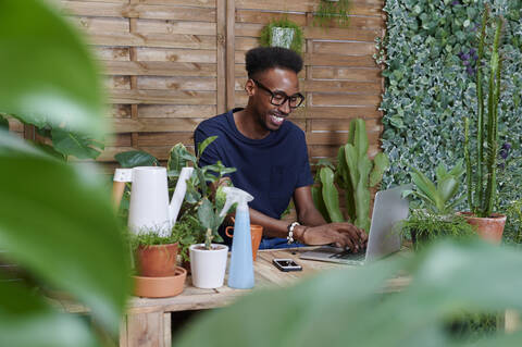 Lächelnder junger Mann mit Laptop auf seiner Terrasse, lizenzfreies Stockfoto