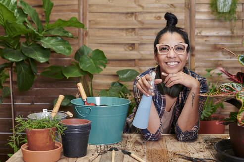 Porträt einer lächelnden jungen Frau bei der Gartenarbeit auf ihrer Terrasse - IGGF01387