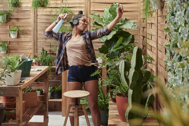 Glückliche junge Frau tanzt auf ihrer Terrasse bei der Gartenarbeit - IGGF01395