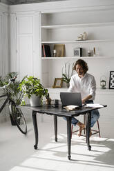 Man sitting at table at home using laptop - GIOF07484