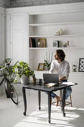 Man sitting at table at home using laptop - GIOF07485