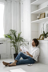 Man sitting on the floor at home reviewing papers - GIOF07499