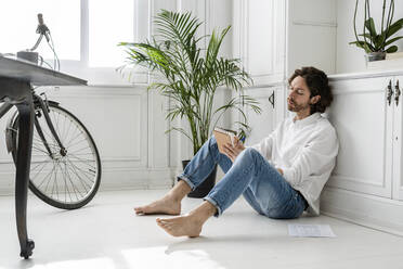 Man sitting on the floor at home taking notes - GIOF07504