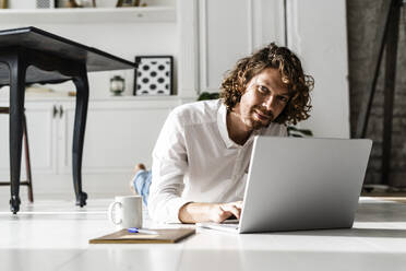 Porträt eines Mannes, der zu Hause auf dem Boden liegt und einen Laptop benutzt - GIOF07509