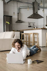 Lächelnder Mann, der zu Hause auf dem Boden liegt und einen Laptop benutzt - GIOF07514