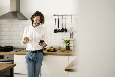 Mann hält Glas Orangensaft und Handy in der Küche zu Hause - GIOF07525