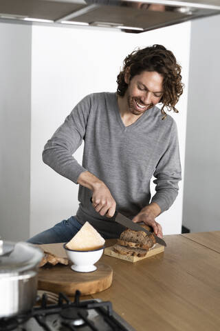 Mann schneidet Brotscheiben in der Küche zu Hause, lizenzfreies Stockfoto