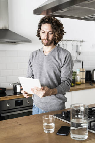 Mann benutzt Tablet in der Küche zu Hause, lizenzfreies Stockfoto