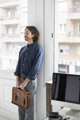Mann hält Tasche in einem Atelier und lehnt sich gegen das Fenster - GIOF07549