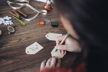 Young woman writing Christmas gift tags - MOMF00791