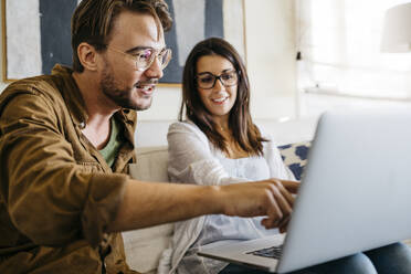 Man and woman sitting on couch using laptop together - JRFF03840