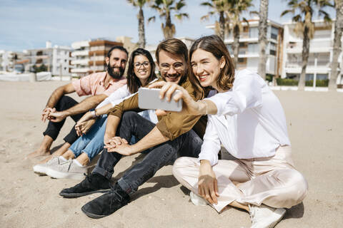 Glückliche Freunde sitzen am Strand und machen ein Selfie, lizenzfreies Stockfoto