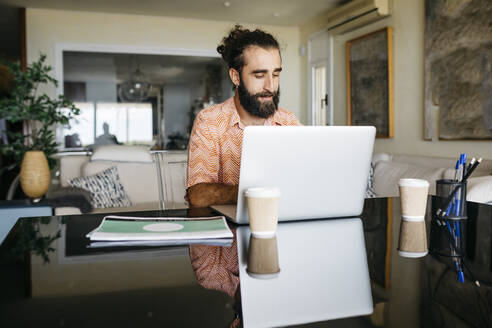 Mann arbeitet zu Hause am Tisch mit Laptop - JRFF03868