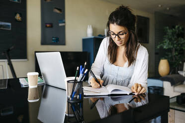 Woman working on table at home taking notes - JRFF03871