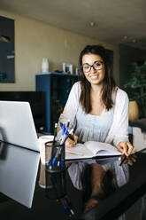 Portrait of smiling woman working on table at home - JRFF03872