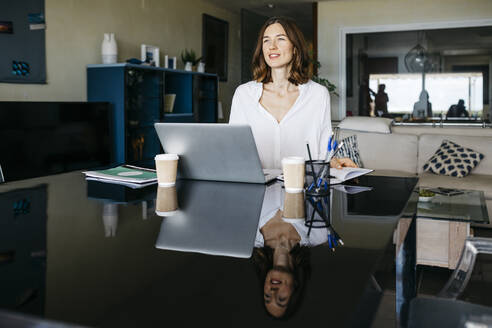 Woman working on table at home with notebook and laptop - JRFF03874