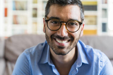 Portrait of happy young man wearing glasses at home - MGIF00838